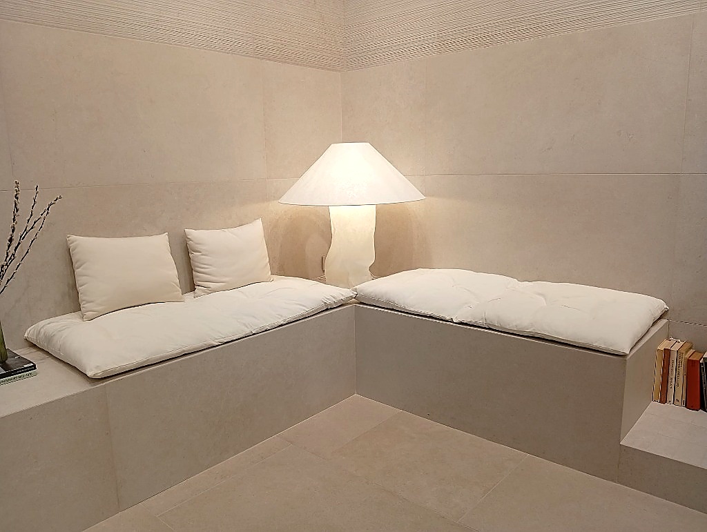 Angolo lounge interamente rivestito in gres porcellanato beige minimale con luce calda e accogliente